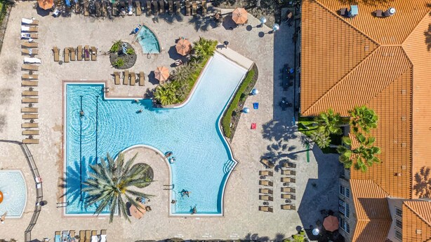 Eine Vogelperspektive auf ein Resort mit einem großen Schwimmbecken, Liegestühlen und einer überdachten Sitzgelegenheit.