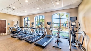 Ein Fitnessstudio mit Laufbändern, Crosstrainern und Fahrrädern, die in Reihen angeordnet sind.