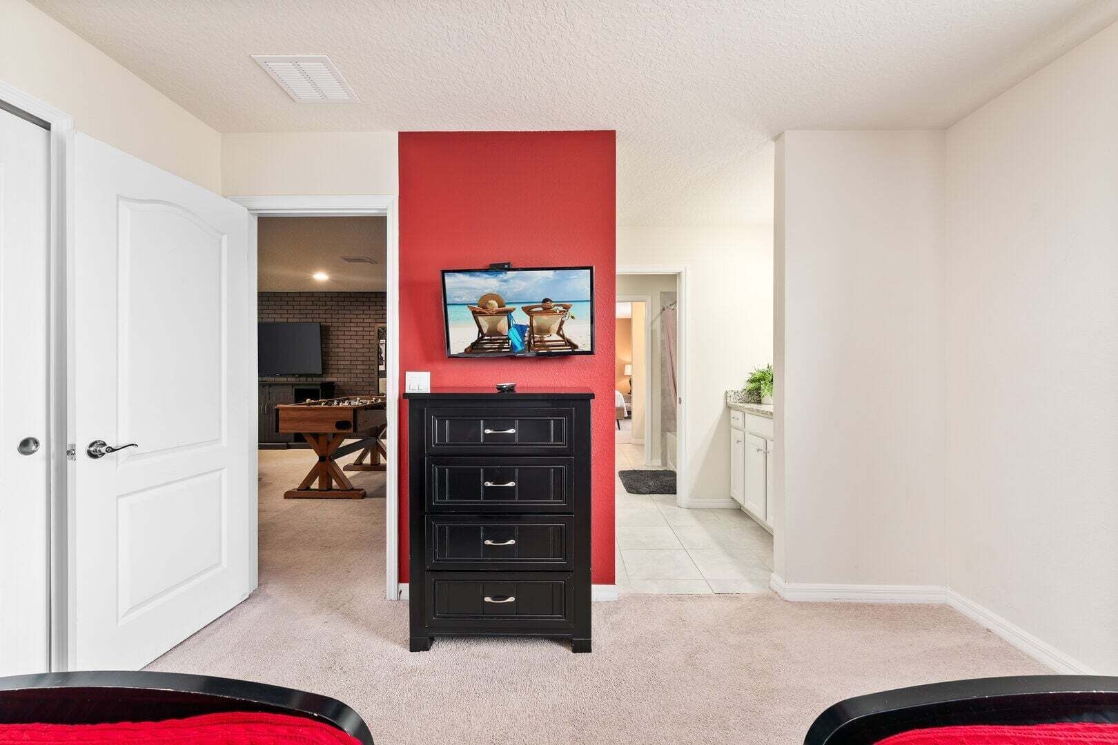 Un couloir avec un mur d’accent rouge, une commode noire à tiroirs et un téléviseur fixé au-dessus.