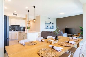 Eine moderne Küche mit weißen Schränken, einer schwarzen Rückwand und einem Essbereich mit einem Holztisch, der mit gewebten Tischsets und einer Blumenvase dekoriert ist.