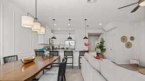 Uma cozinha moderna com armários brancos, uma mesa de jantar com cadeiras e iluminação pendente.