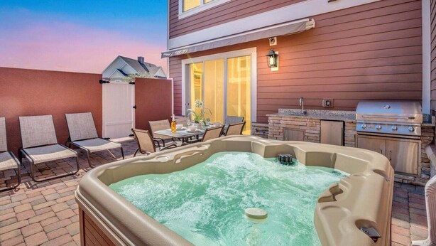 Un patio trasero con jacuzzi, mobiliario exterior y una parrilla.