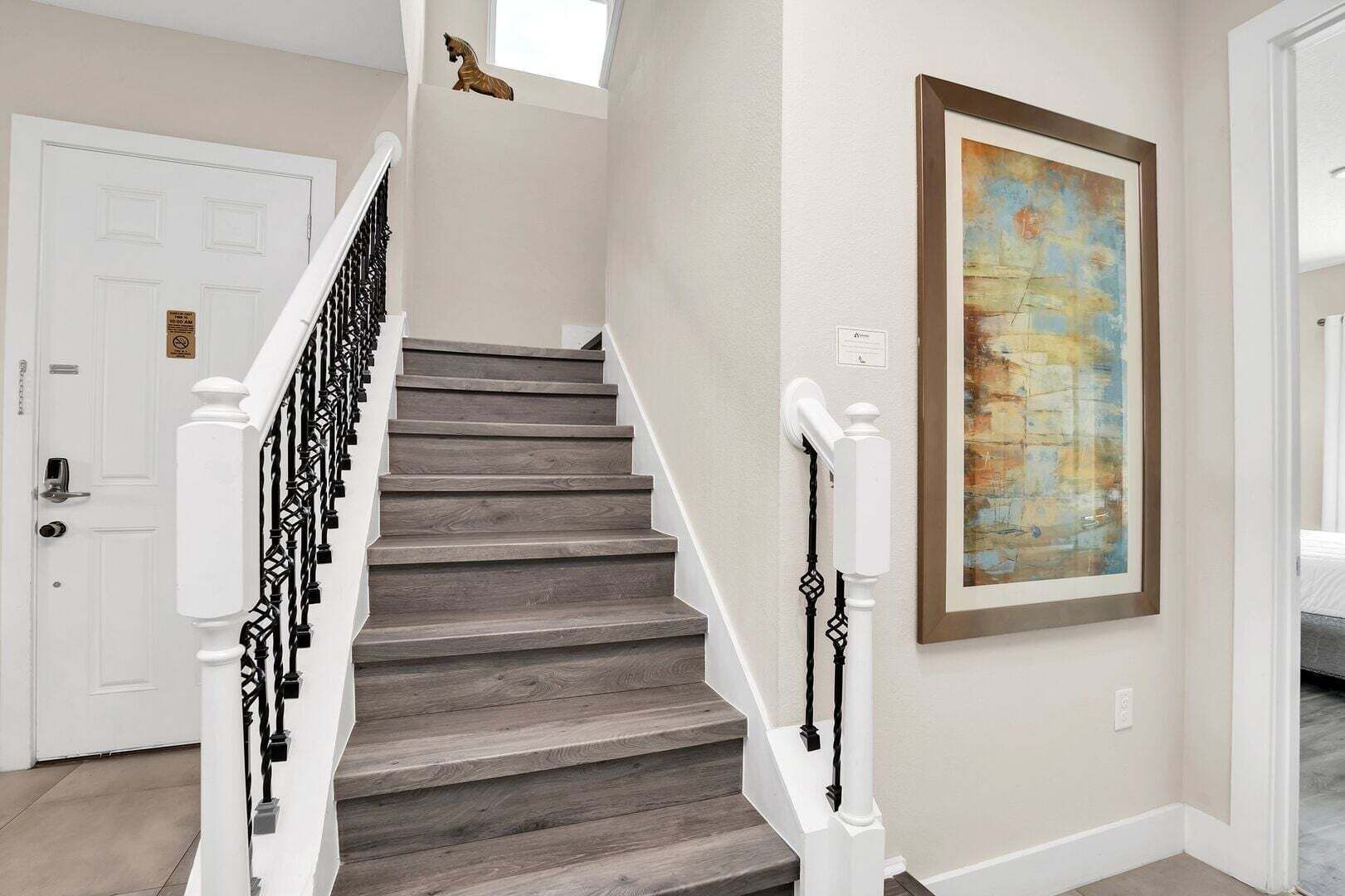 Una escalera con barandilla blanca, una puerta con un letrero y un cuadro abstracto enmarcado en la pared.
