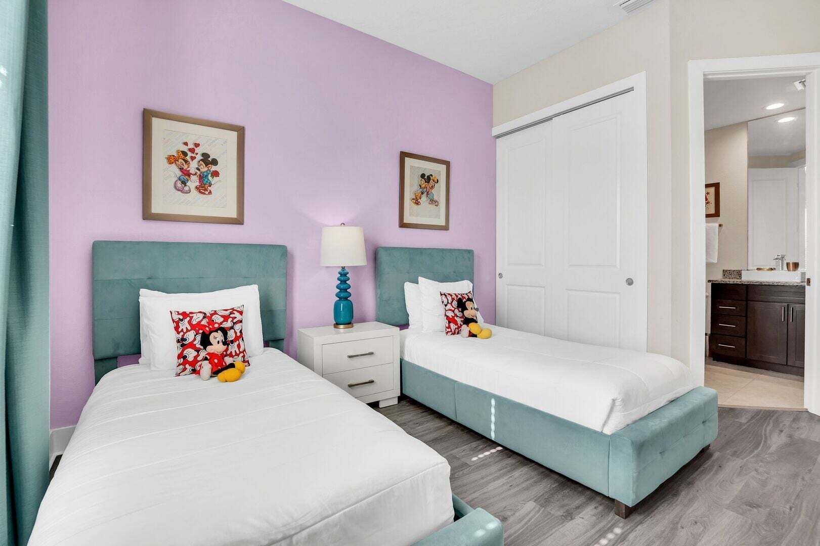 Camera d'albergo con due letti, un comodino con lampada, una porta e vista sulla cucina.