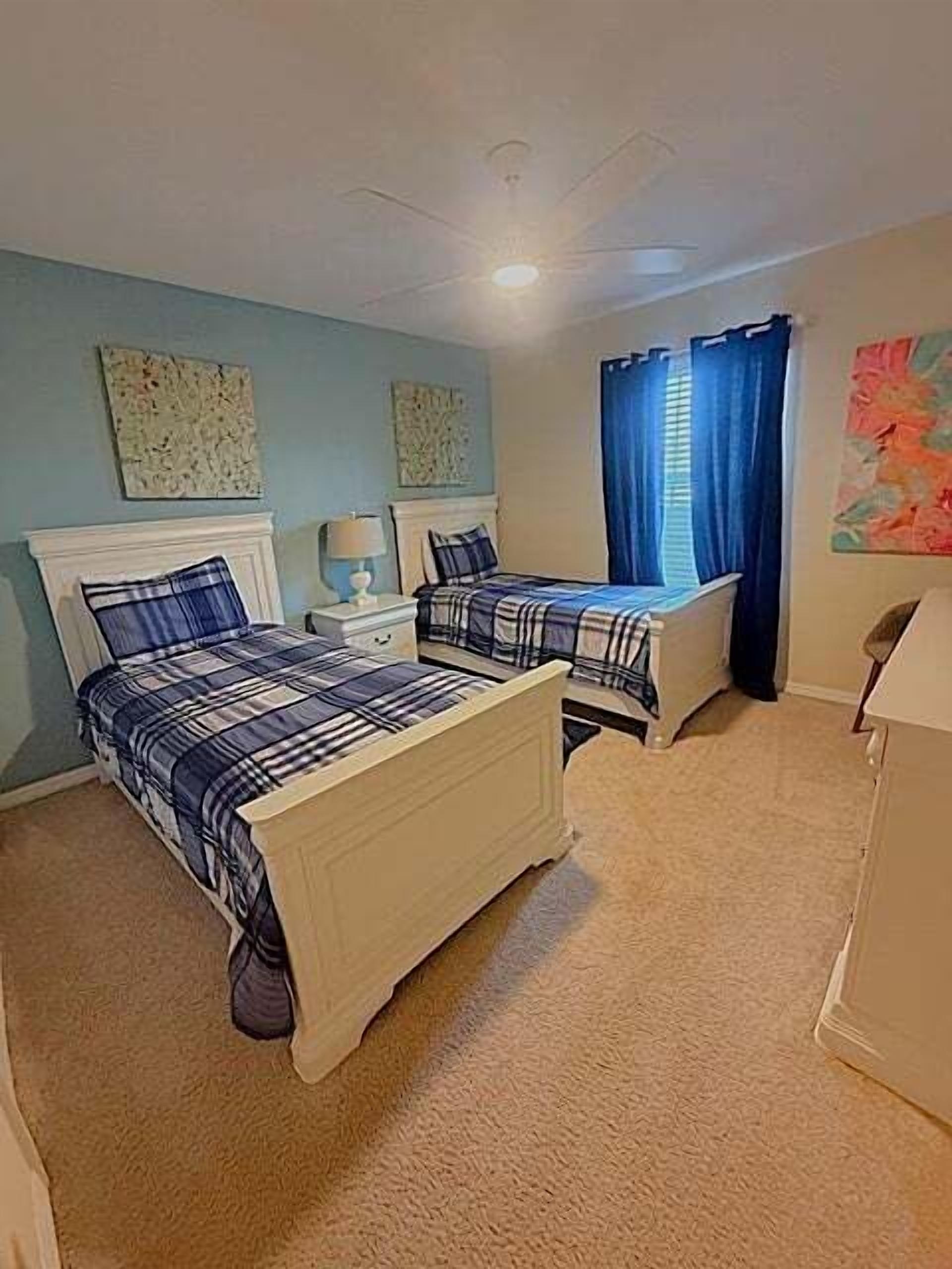 A bedroom with two beds, a nightstand, a lamp, and a ceiling fan.