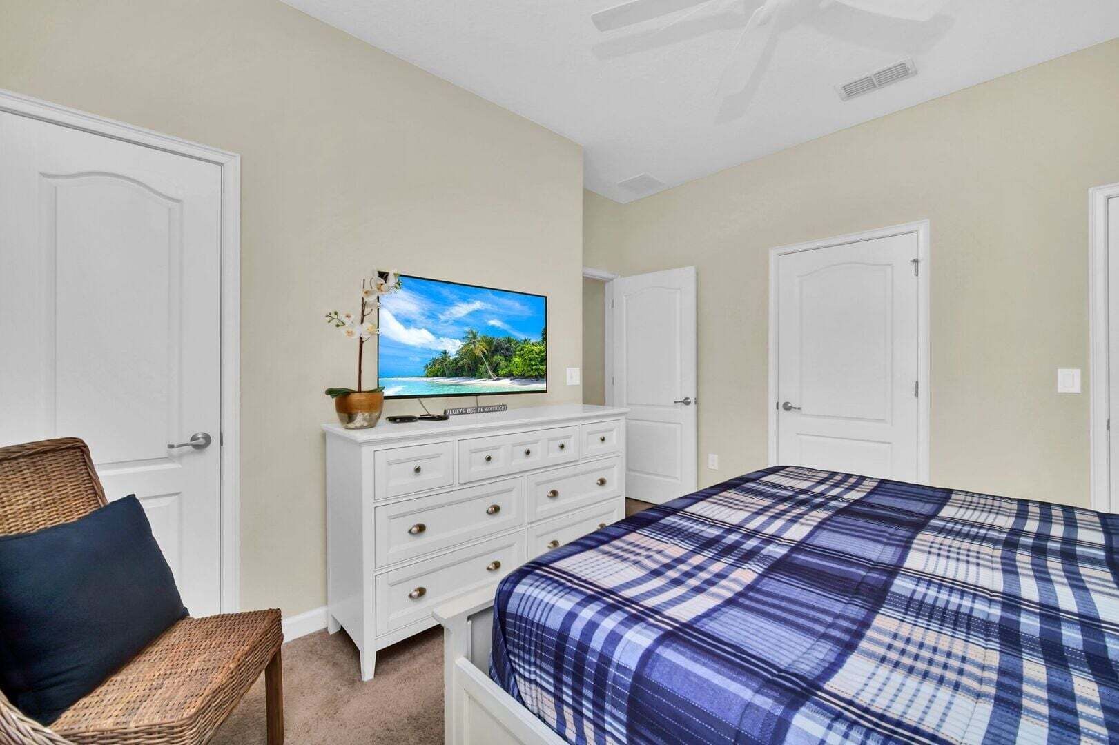 A bedroom with a bed, dresser, television, and a wicker chair.