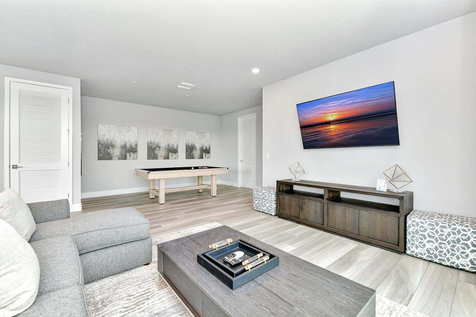 Ein modernes Wohnzimmer mit Billardtisch, grauem Sofa, Couchtisch und einem großen, an der Wand montierten Fernseher.