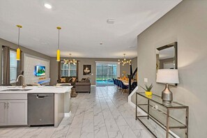 A modern kitchen with a built-in dishwasher, a dining area with a glass table, and a living room with a sofa and TV. - Mickey Mouse Clubhouse 8min to Disneyworld Pool/spa Sleeps 20 St102 (Kissimmee)