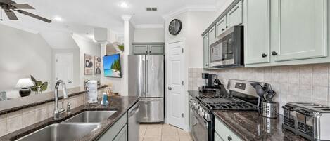 Una cocina moderna con encimeras de granito, electrodomésticos de acero inoxidable y armarios color verde claro.