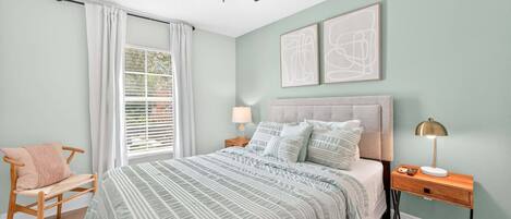 A bedroom with a bed, a nightstand, a chair, a ceiling fan, and artwork on the wall.