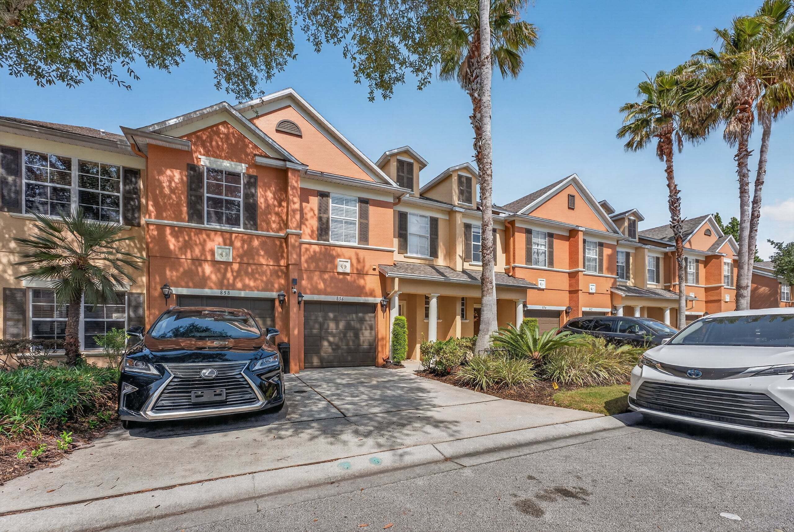 A row of townhouses with attached garages, palm trees, and a clear blue sky.