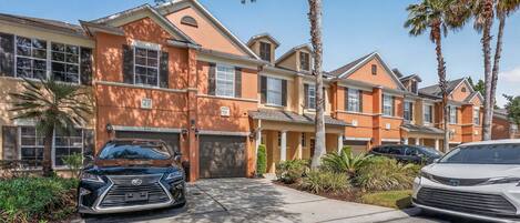 A row of townhouses with attached garages, palm trees, and a clear blue sky.