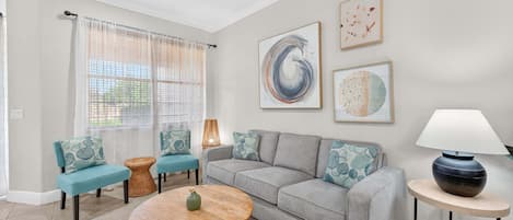 En stue med en grå sofa, teal farvede lænestole, et rundt sofabord, en loftsvifte og kunst på væggen.