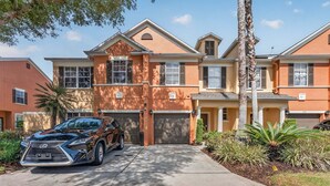 A multi-story residential building with a driveway, parked car, and well-maintained landscaping. - Cozy 3BR Townhome 5 Miles From Disney (Kissimmee)