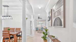 A spacious living area with a dining table, chairs, a ceiling fan, and a large window. - Cozy 3BR Townhome 5 Miles From Disney (Kissimmee)