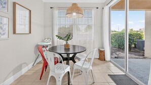 A dining area with a round table, white chairs, a hanging light fixture, and a view through a glass door. - Cozy 3BR Townhome 5 Miles From Disney (Kissimmee)