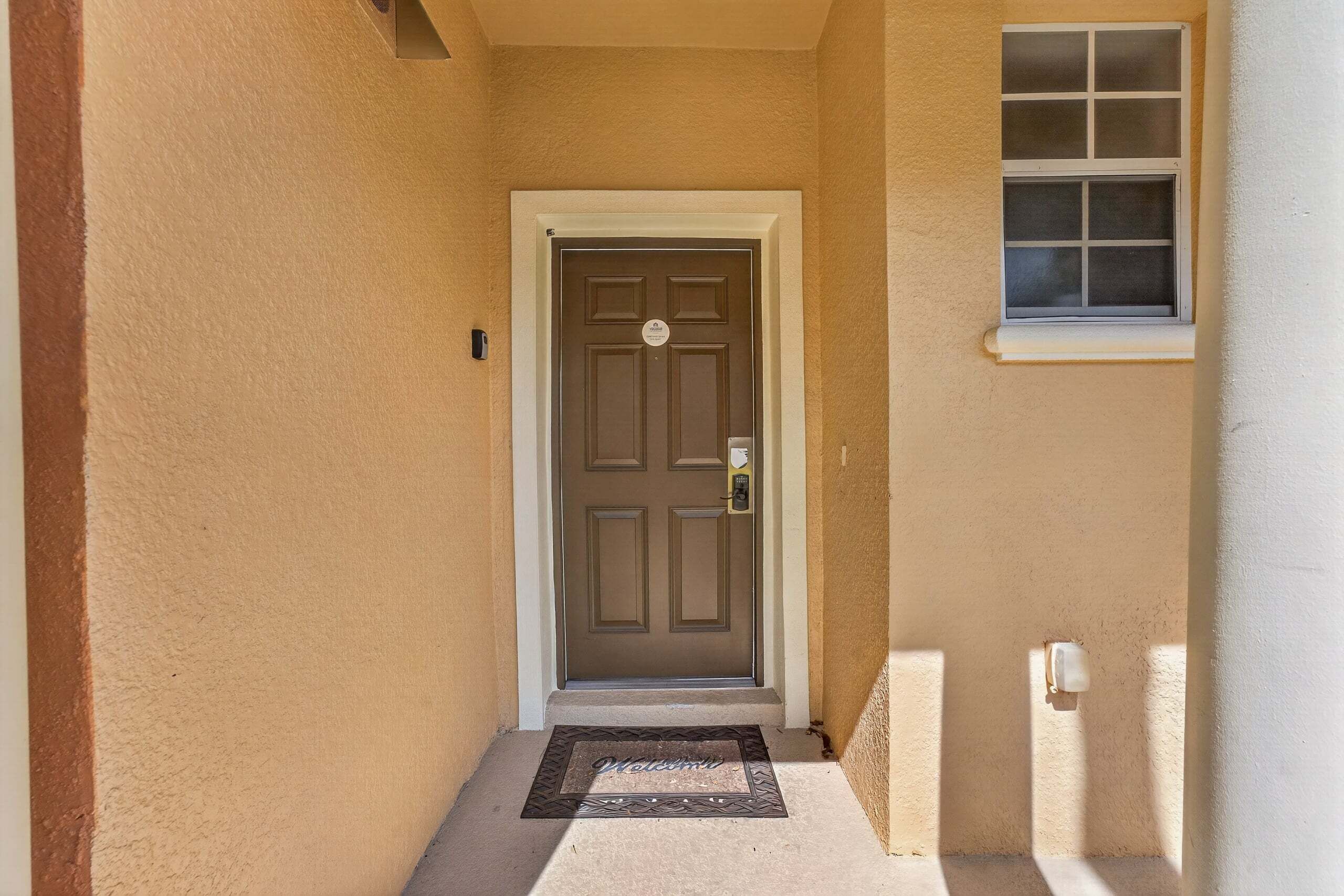 A front door with a doormat, a small window above it, and a wall-mounted light switch.