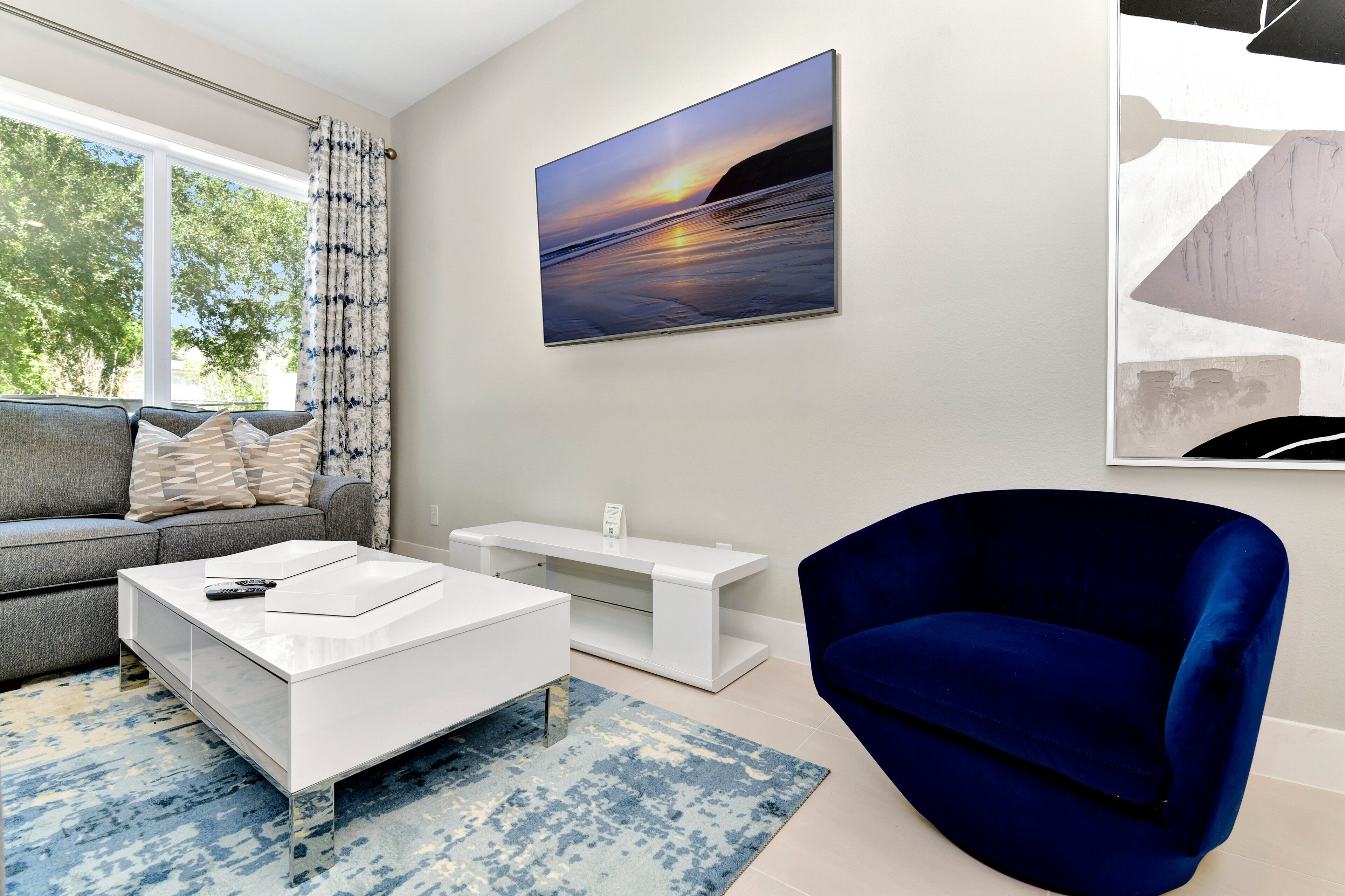 A modern living room with a sofa, a coffee table, a blue armchair, and a painting of a sunset.