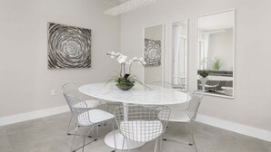 A modern dining area with a round table, wire mesh chairs, and abstract wall art. - Precious Villa - 5 min to Disney (Kissimmee)
