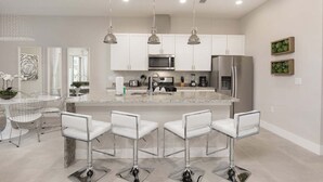 A modern kitchen with white cabinets, stainless steel appliances, and a central island with bar stools. - Precious Villa - 5 min to Disney (Kissimmee)
