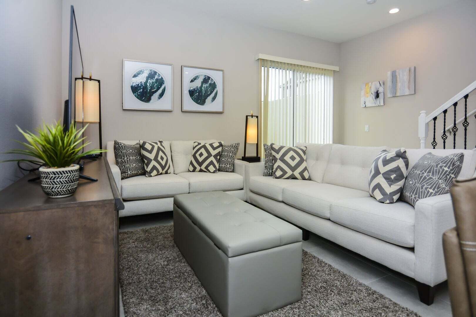 Una sala moderna con un sofá modular, una mesa de centro y almohadones decorativos. Hay cuadros enmarcados en la pared y una lámpara de pie.