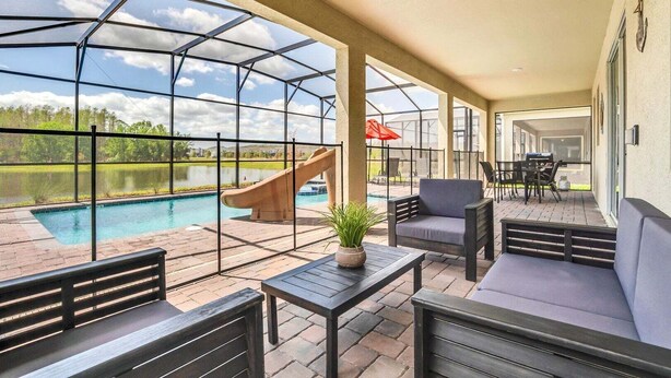 A covered patio with a pool, seating, and a slide. - Magical Mickey Home 8min->disney! (Kissimmee)
