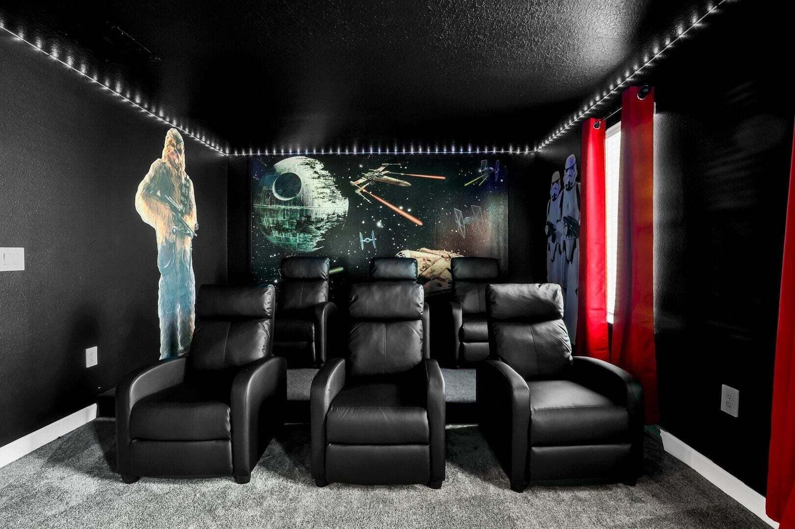 Un cine en casa con una pantalla grande, sillones de cuero negro y decoración temática de Star Wars.