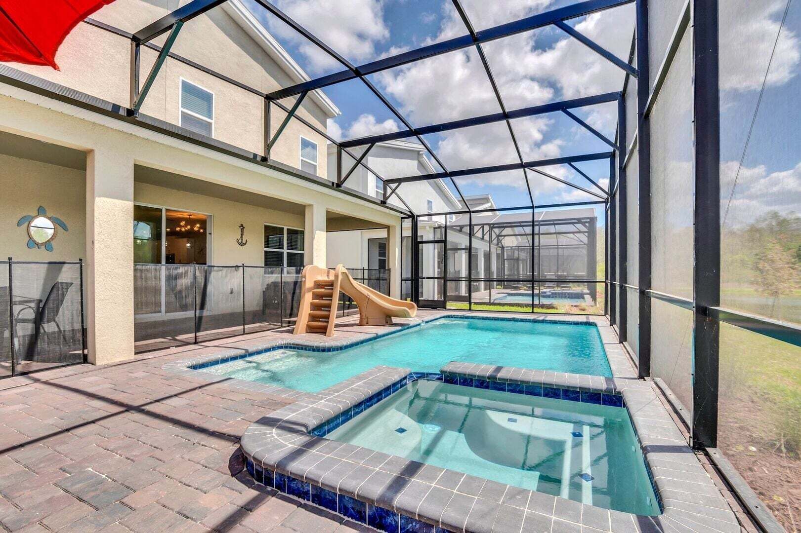 A covered outdoor swimming pool with a slide, a hot tub, and a view of a hot tub in the background.