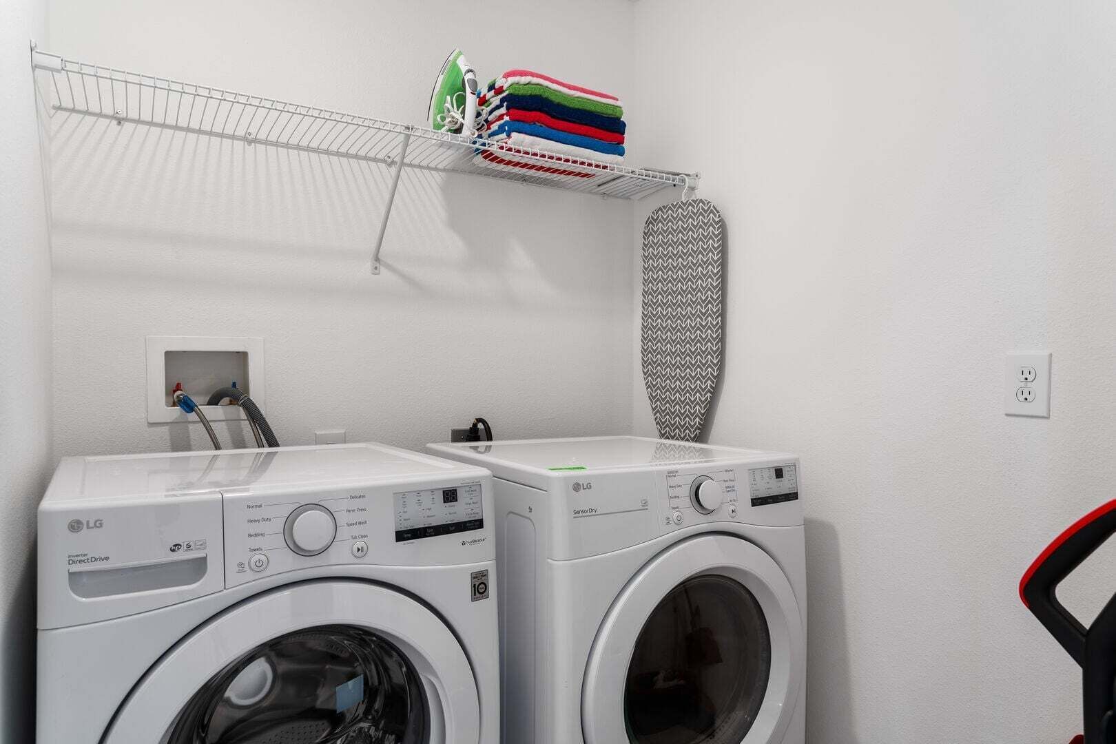 Un espace buanderie équipé de deux machines à laver LG, d’un étendoir sur lequel sont pliés des vêtements et d’une planche à repasser à motifs.