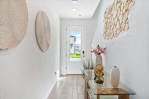 Ein Flur mit einem Glastisch, Wanddekoration und Blick auf ein Haus durch eine Tür.