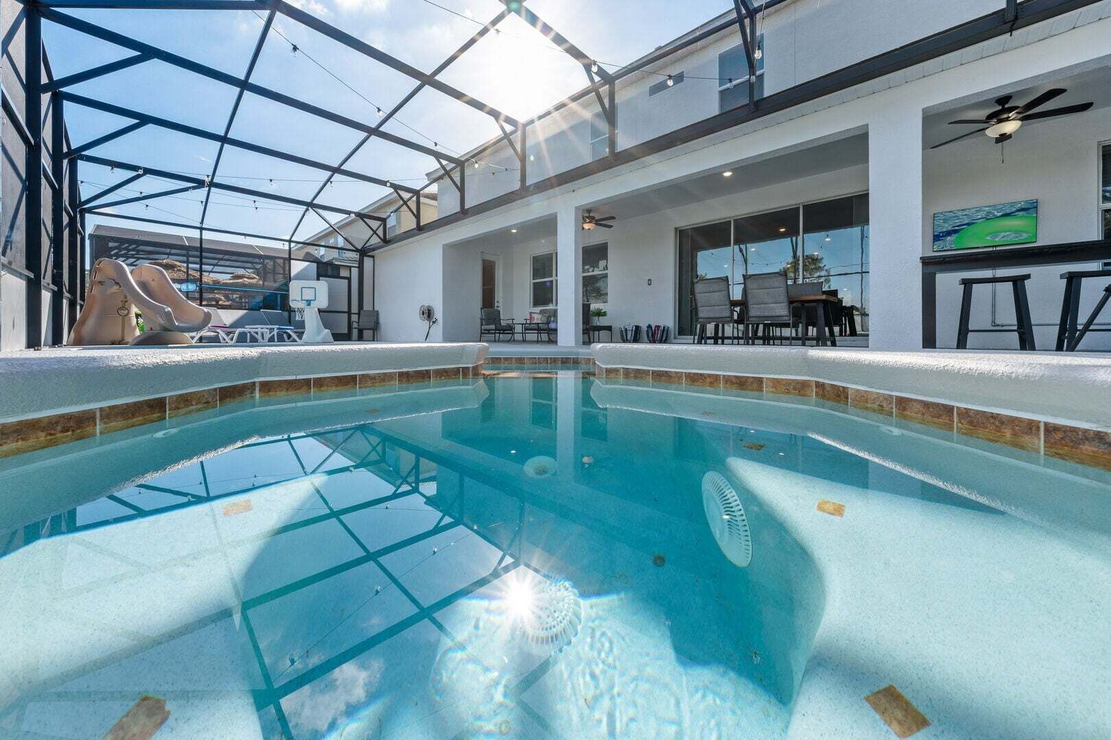 An indoor swimming pool with a glass ceiling, a slide, and a seating area with chairs and tables.