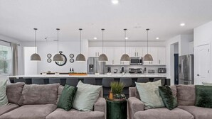 Una cucina moderna con illuminazione a sospensione, un'isola centrale e un'area salotto con divani.