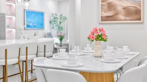 Een moderne eetruimte met witte stoelen, een marmeren tafel en een vaas roze bloemen.
