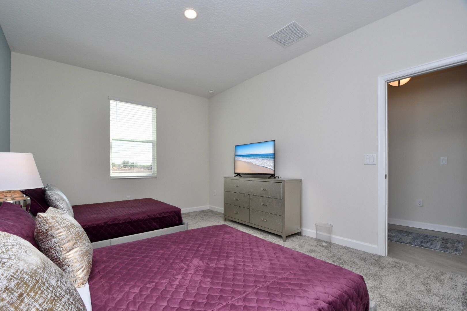 A bedroom with two beds, a dresser, a television, and a window.