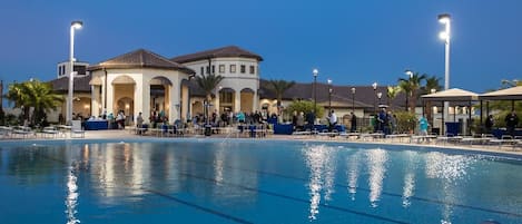 A swimming pool with lounge chairs and umbrellas, a building with arches, and palm trees.