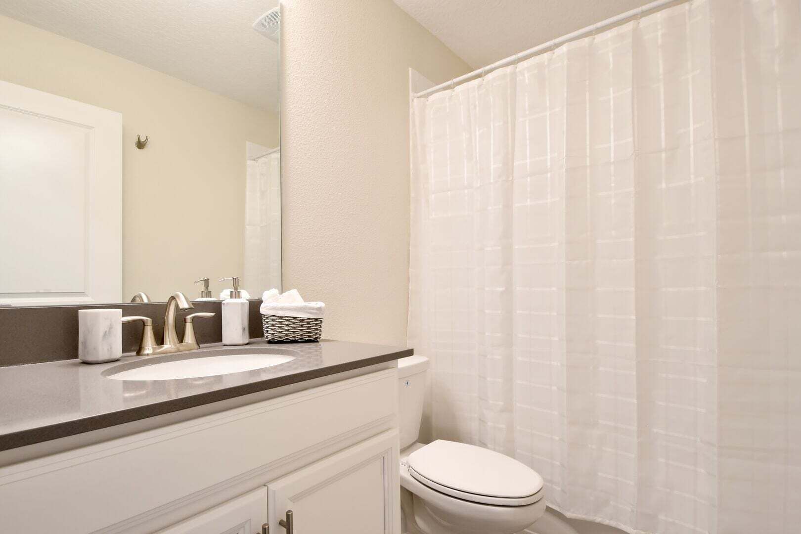 A bathroom with a sink, mirror, toilet, and a shower curtain.
