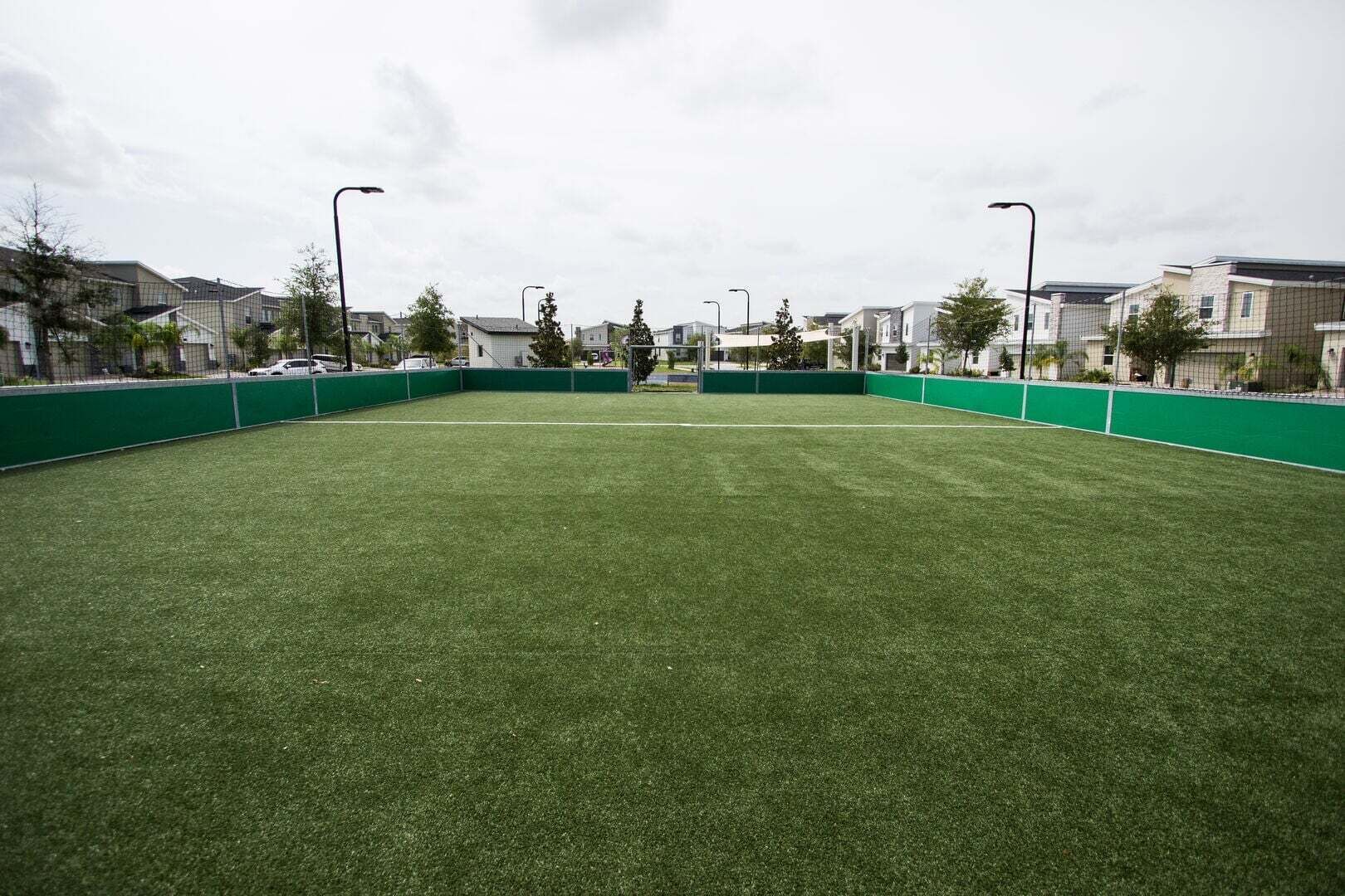 A sports field with green fencing and street lamps.