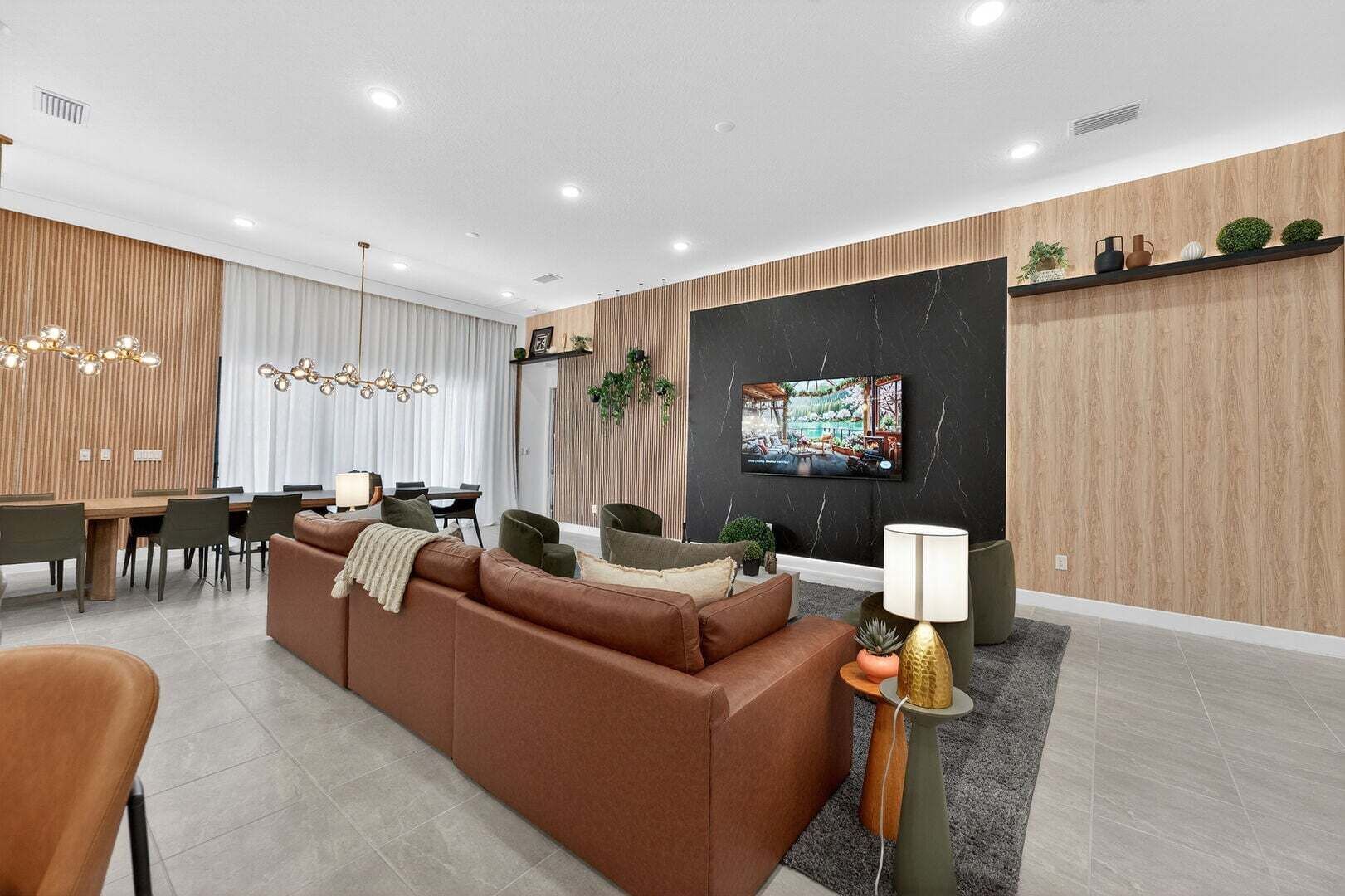 A modern living room with a sofa, dining table, chairs, and a TV mounted on the wall.