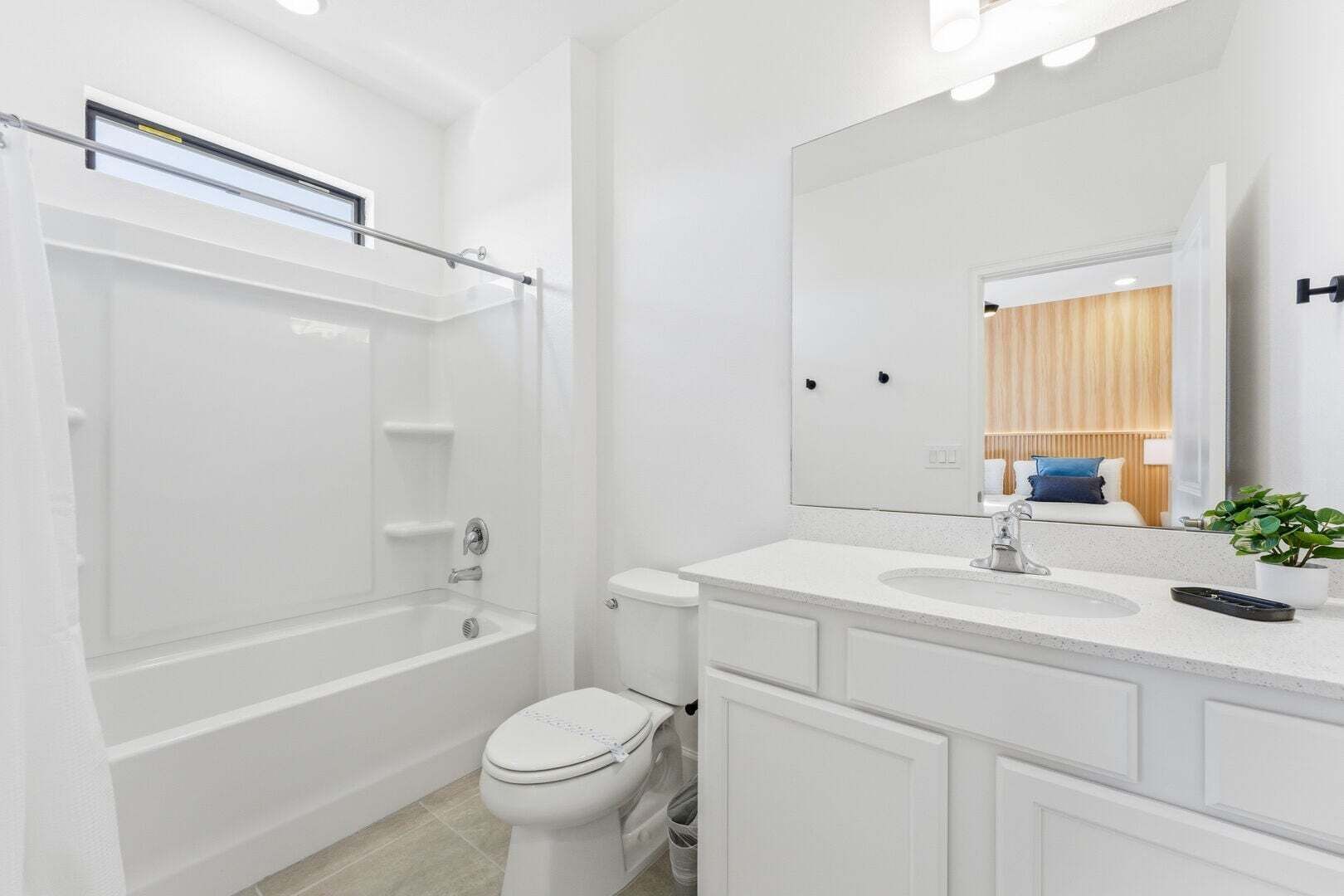 A modern bathroom with a bathtub, toilet, vanity with a mirror, and a potted plant.