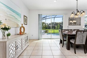 A modern dining area with a view of a swimming pool and a landscaped backyard. - Lakeview Home Sleeps 25 (Kissimmee)