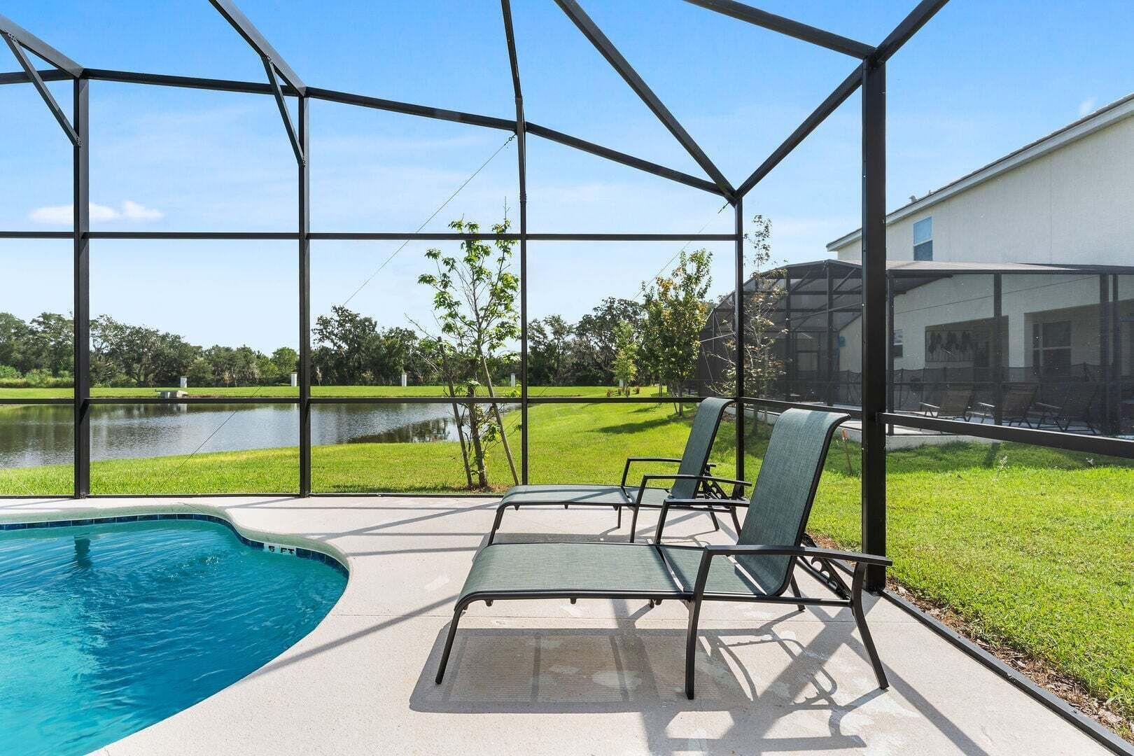 Uma área externa coberta com piscina, cadeiras e vista para um lago e vegetação.