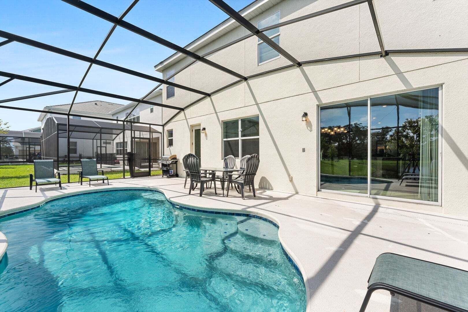 A swimming pool with a covered patio area, outdoor furniture, and a view of a neighboring house.