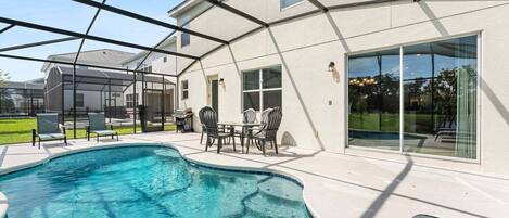 A swimming pool with a covered patio area, outdoor furniture, and a view of a neighboring house.