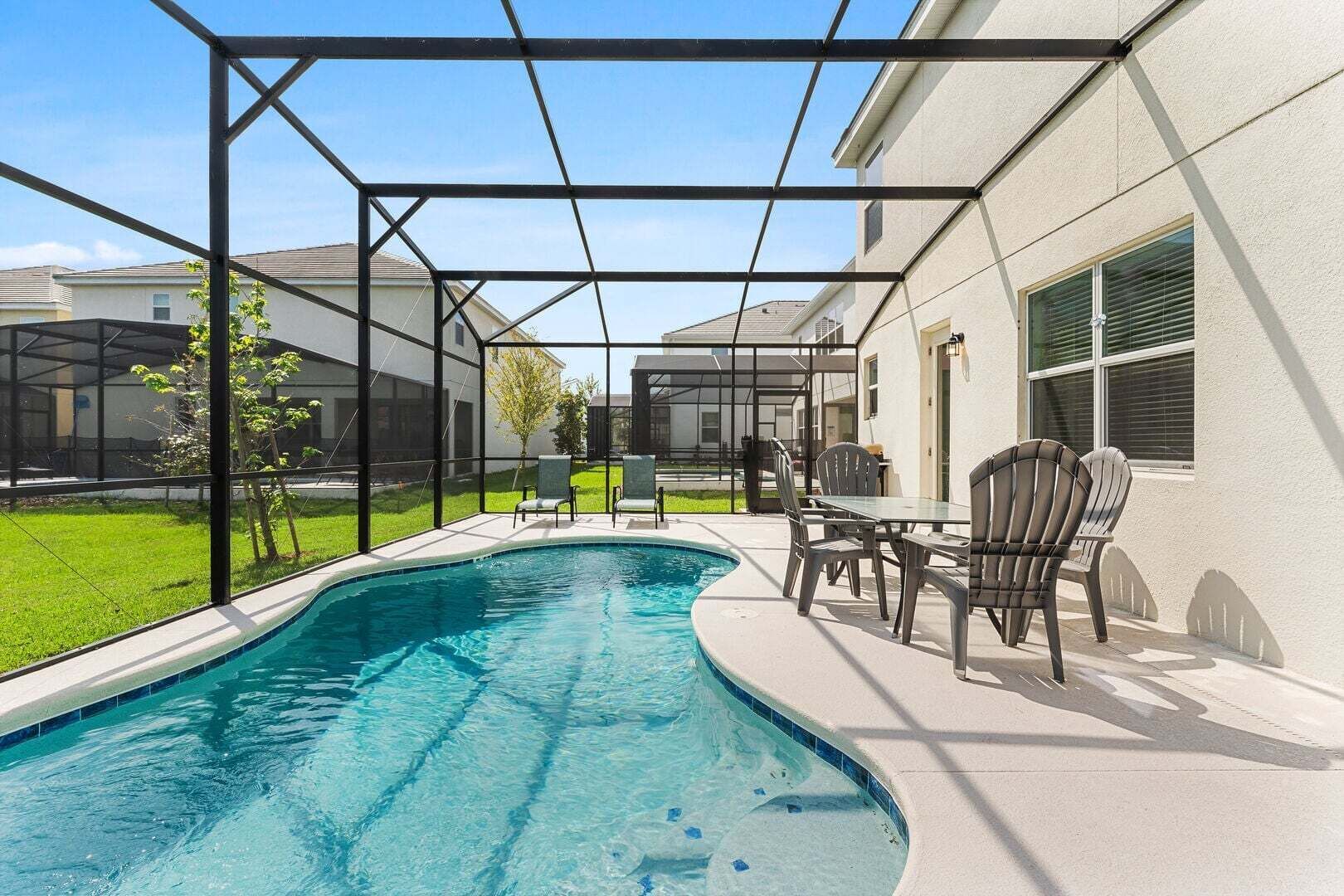 A swimming pool with a glass enclosure, outdoor seating, and a view of neighboring houses.