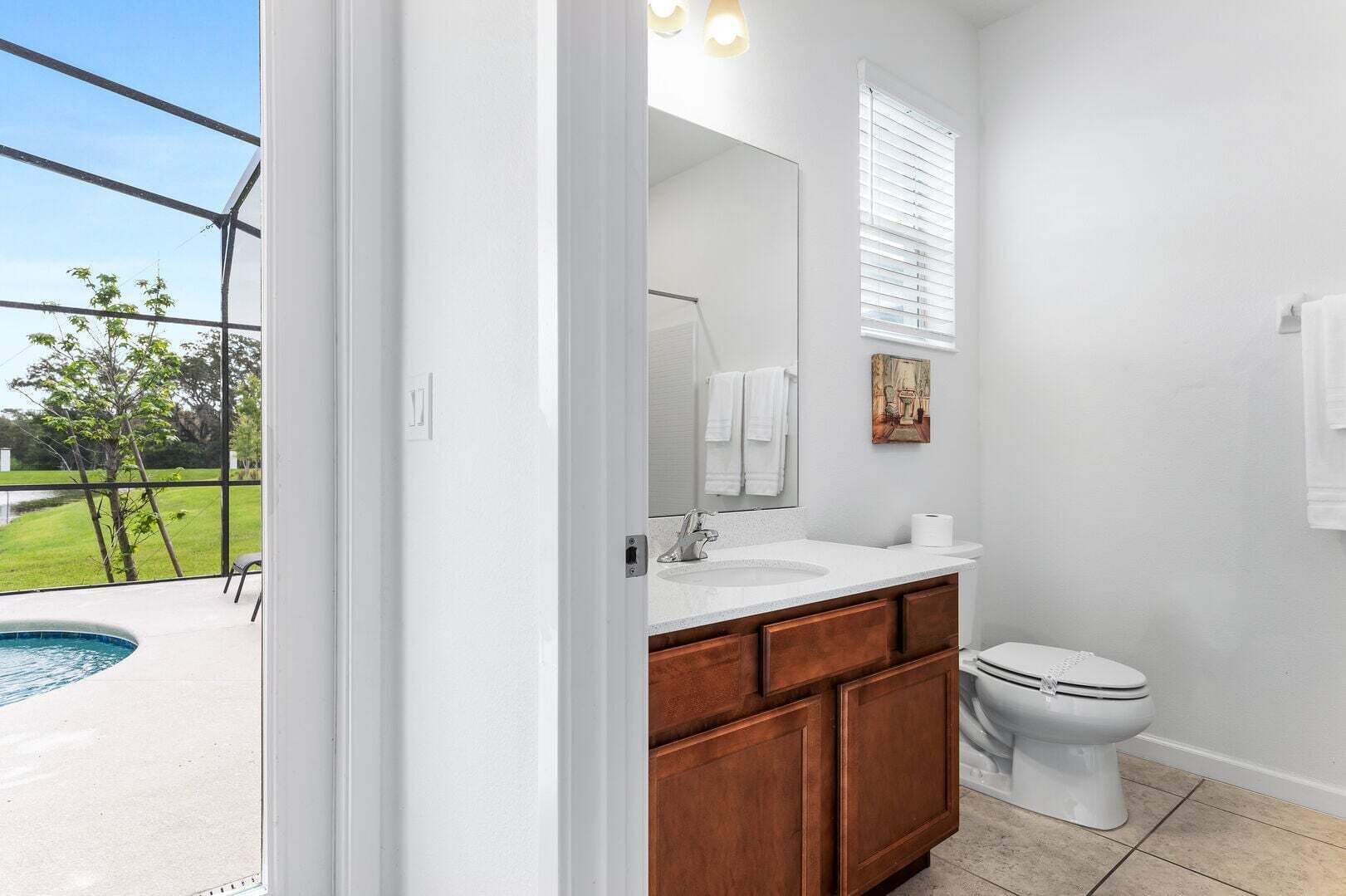 A bathroom with a large window, a sink, a toilet, and a small pool visible outside.