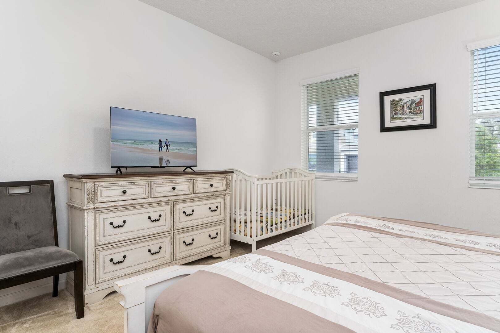 Une chambre à coucher comprenant un lit, une commode, un berceau, une chaise et un téléviseur.