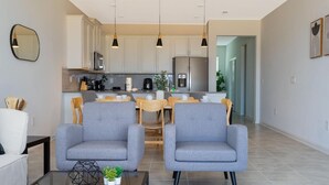 Een moderne woonkamer met twee grijze fauteuils, een glazen salontafel, en een eethoek met een houten tafel en stoelen.