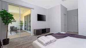 Een moderne slaapkamer met een bed, een televisie, een schuifdeur naar een balkon en een plant in pot.