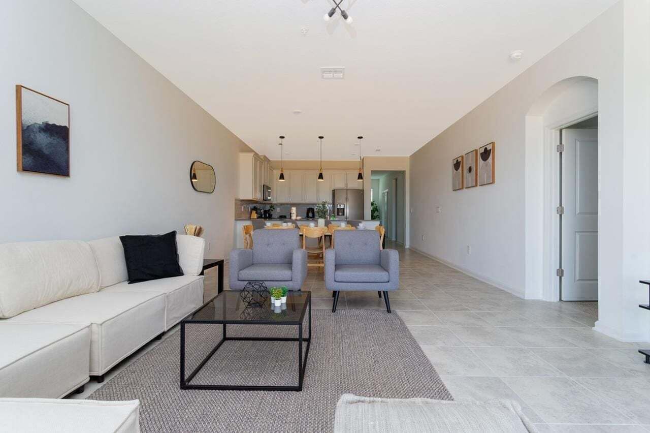 Una sala de estar moderna con un sofá, dos sillones, una mesita de centro y una cocina al fondo.