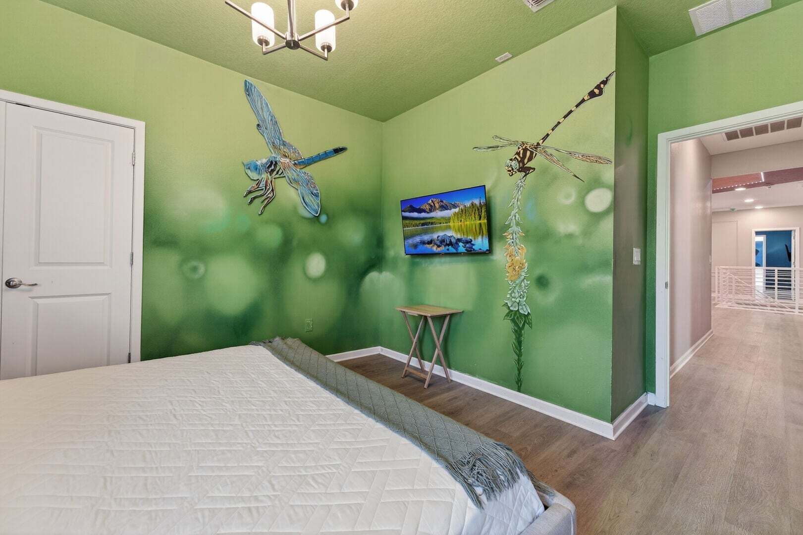 A bedroom with a bed, a painting, and a wall mural of a dragonfly.